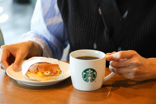 [20251123] 스타벅스 사진자료3_고객이 '모닝 세트'로 구입한 '베이컨 체다 & 오믈렛 샌드위치'와 '카페 아메리카노'를 즐기는 모습